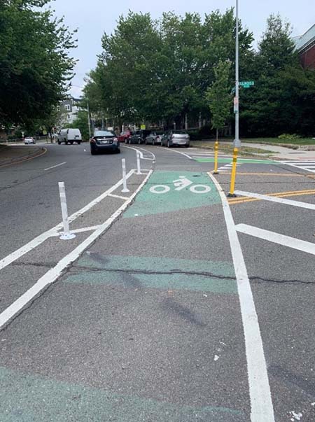 A separated bike lane that has plastic bollards on each side. The lane also has an image of a bicyclist painted on the pavement.