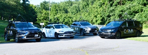 Four vehicles are parked on an asphalt surface with grass and trees in the background.