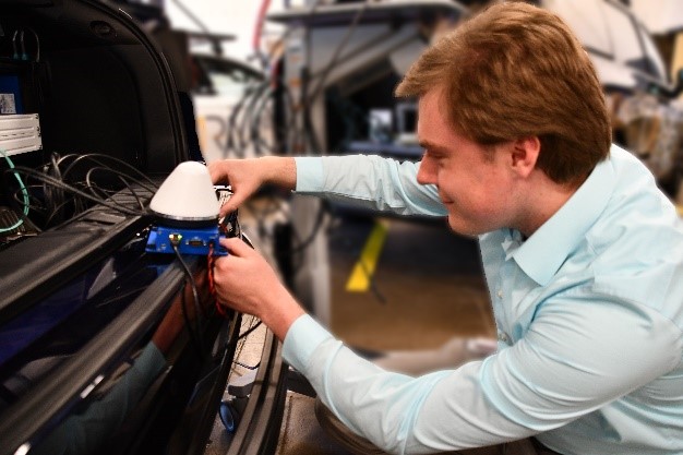 A man installs an onboard unit in the trunk of a vehicle.