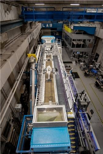 The photo shows a birds-eye view of the FHWA Hydraulics Laboratory. The tilting flume is on the left. Next to the tilting flume is the computational fluid dynamics (CFD) station, ex situ scour testing device (ESTD), in situ scour testing lab sump device, and the force balance flume (from top to bottom). From top-to-bottom on the right: soil sample preparation station, presentation station, and the fish passage culvert flume.