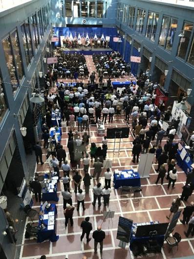 Attendees of the Research Showcase listen to speakers on the main stage and browse exhibit tables on each side and in the middle of the hall.