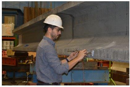 A man in a hardhat takes measurements on a concrete beam.