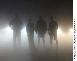 people standing in the dark illuminated by headlights