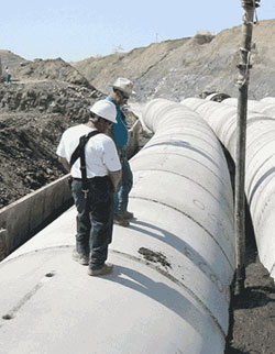 Workers inject flowable fill containing recycled foundry sand to fill the spaces between the pipelines on this roadway construction project.