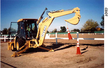 Participating in one of the many demonstrations at the 2005 Colorado Construction Career Days event, a student operates a backhoe to pick up and place one traffic cone on top of another cone. (Photo Credit: CDOT)