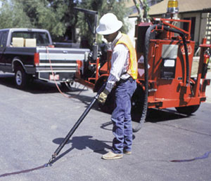 A worker is shown sealing a pavement crack. Crack sealing is one of a variety of cost-effective, thin-surface treatments that can help preserve and extend the service life of pavement.