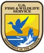 FWS Logo, which features a mallard duck flying above a lake from which a bass fish is jumping. There is a mountain peak and a large sun in the background. It reads, "US Fish & Wildlife Service."