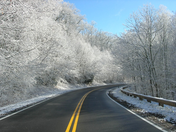 This is a photo of a road in Great Smoky National Park. It has recently snowed. The road is clear. The sky is blue. The forest on each side of the road is covered in snow.