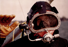 This photo is a headshot of Mike Jones waving while wearing scuba diving equipment.
