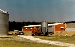 This is a photo of Mike Jones' family farm in the 1980s. It pictures a silo to the left and a red warehouse to the right.
