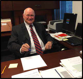 Title: Photo of Office Director, Virgil Pridemore - Description: This is a picture of Virgil Pridemore, HEPR Office Director, sitting at his desk. There are papers and a laptop on the desk. Virgil is smiling.