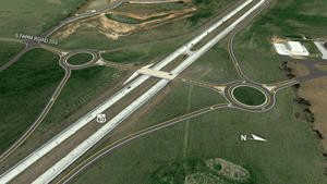 Satellite image of a highway interchange. Four lanes of divided highway run diagonally acros the image. Exit and entrance ramps connect to each side of the highway.