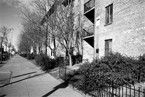 Edificio de apartamentos - Description: Esta foto en blanco y negro es de un edificio de apartamentos de ladrillo con una acera ancha situada a lo largo del edificio en el lado izquierdo de la imagen.