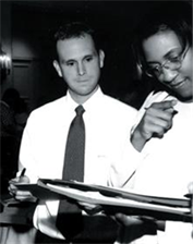 Profesionales trabajando - Description: Esta es una imagen en blanco y negro de un hombre y una mujer que miran un cuaderno.