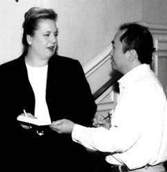 Profesionales teniendo una conversación - Description: Esta es una foto en blanco y negro de una mujer y un hombre conversando el uno con el otro. La mujer está sosteniendo cuaderno de notas y un bolígrafo. Ella está entregando el cuaderno de notas al hombre.