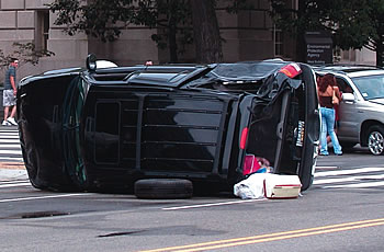 Photo showing a black S U V on its side in the middle of an intersection.
