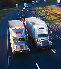 Photo showing two large transport trucks traveling along a highway side by side.