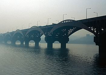Photo showing a bridge spanning a river with smog.
