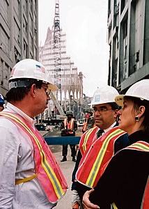 Photo showing three officials in hardhats and a security person outside the remains of the World Trade Center after the attack on September 11th, 2001.