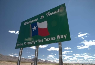 Photo of Texas highway welcome sign saying Welcome to Texas, Drive Friendly – the Texas Way along with an illustration of a Texas flag.. 