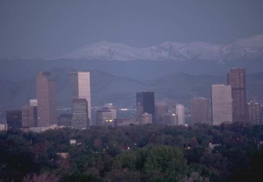 Photo of slightly hazy Denver, CO skyline taken looking west with the Rocky Mountains in the background.