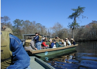 Photo of the multiple members of the scan team sitting in a boat while wearing life jackets as they charter the waters of Blue Elbow Swamp in Texas.