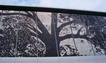 one side of Raleigh’s relatively new convention center. The nearly 9300 square foot display consists of 79,464 light and dark aluminum squares that shift about in the wind, creating multiple variations of the primary image of an oak tree (which has, incidentally, become a symbol for the city). At night, it is backlit by light-emitting diodes that can be programmed in more than a million different colors. 