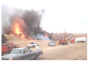 Photo of a wildfire with several fire and police responders and water tanker trucks on the scene.