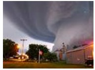 Photograph of a tornado moving toward a series of structures and a light pole.