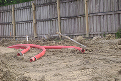 Photo showing bore rod protruding from bore hole and three conduits that will be pulled into the hole.